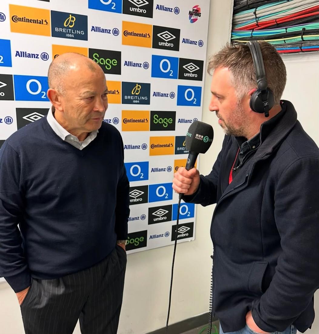 Chris interviewing a coach in front of a sponsor board